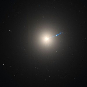 شکل ۱: تصویر کهکشان M87 توسط تلسکوپ فضایی هابل. فوران ماده از سیاه‌چاله‌ی مرکزی کهکشان نیز به رنگ آبی دیده می‌شود (تصویر ترکیبی از نور مرئی و فروسرخ است).