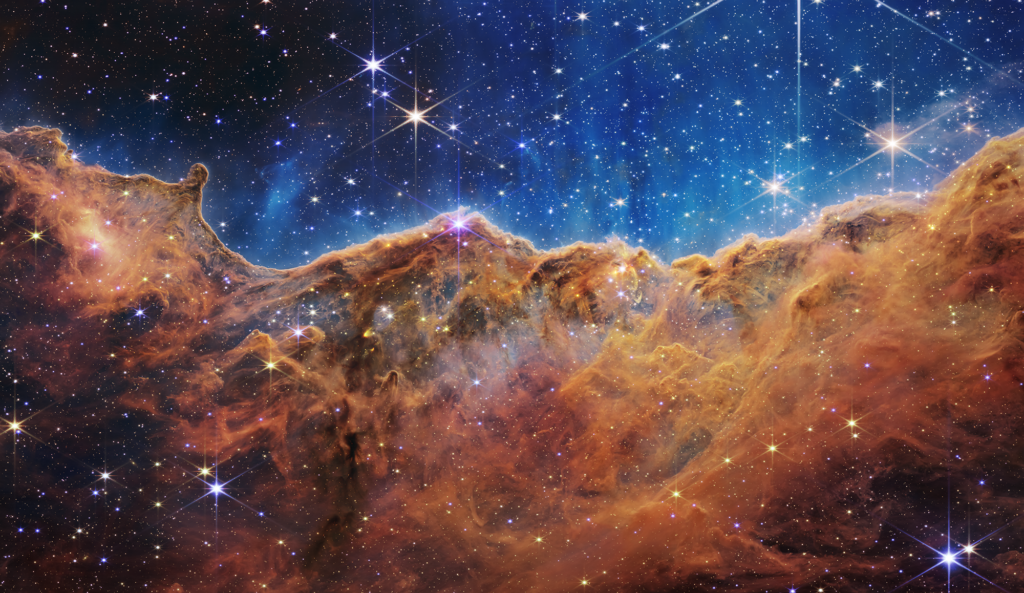 شکل ۱: سحابی حمال (carina) در کهکشان‌ راه‌شیری. این تصویر با دوربین نیرکم گرفته شده است و ابرهای گازی و غباری اطراف محل تولد ستاره‌ها را نشان می‌دهد. Credit: NASA, ESA, CSA, STScI